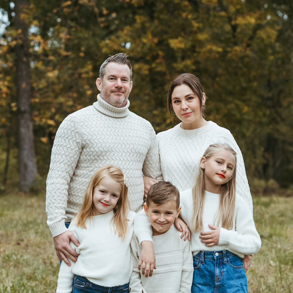 Ben DeMoss, Project Manager with Ridgeline Roofing and Solar of Joplin, Grove, and Bentonville, is standing with his wife and children posing in a field for a family photo.