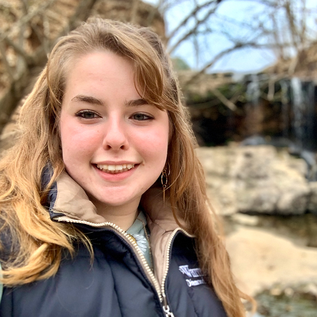 Hannah Lemmermann is a Project Manager with Ridgeline Roofing and Solar of Joplin, MO standing in a wooded area wearing a fall/winter coat.